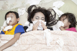 Mother and children with colds lying in bed blowing their noses.