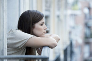 Woman leaning on balcony, looking upset and staring into space.